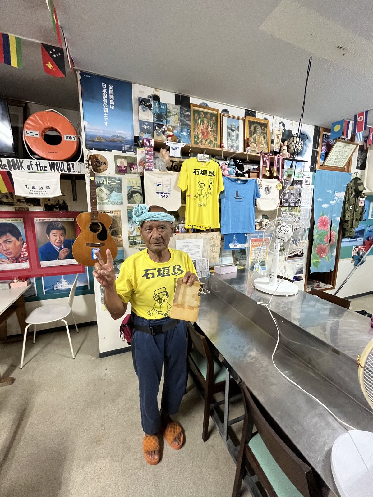 黄色い石垣島Tシャツを着てピースする栄福食堂の店主・通事國浩さん